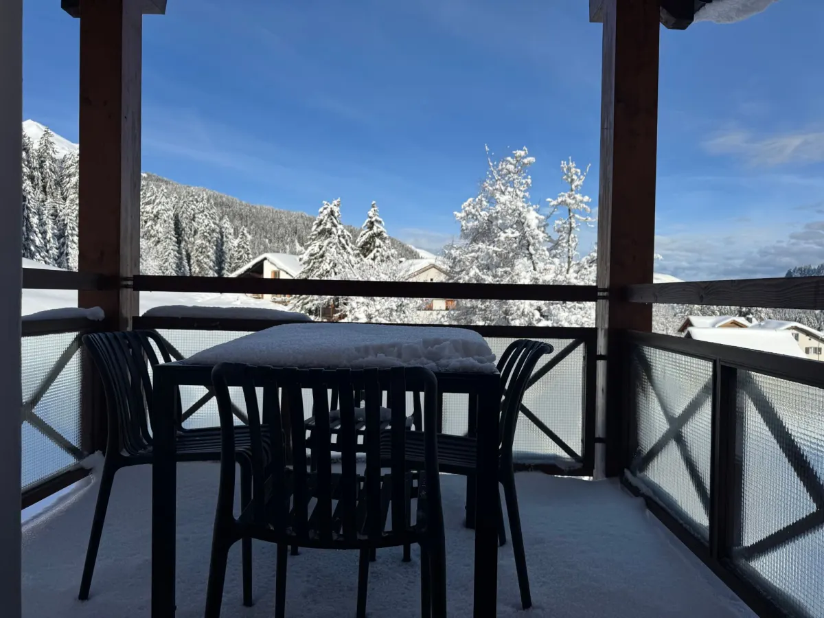 Der Balkon nach einer Neuschneenacht, dahinter verschneite Wälder und Berge